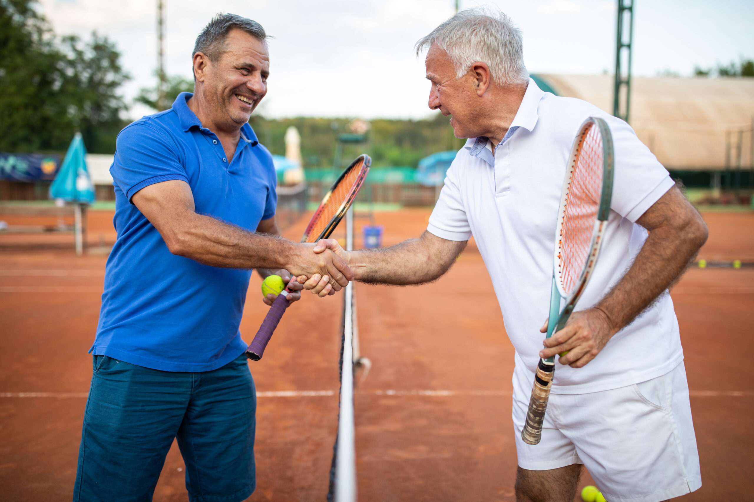 Two friends handshake before they start to play tennis, on tennis court with net between them
